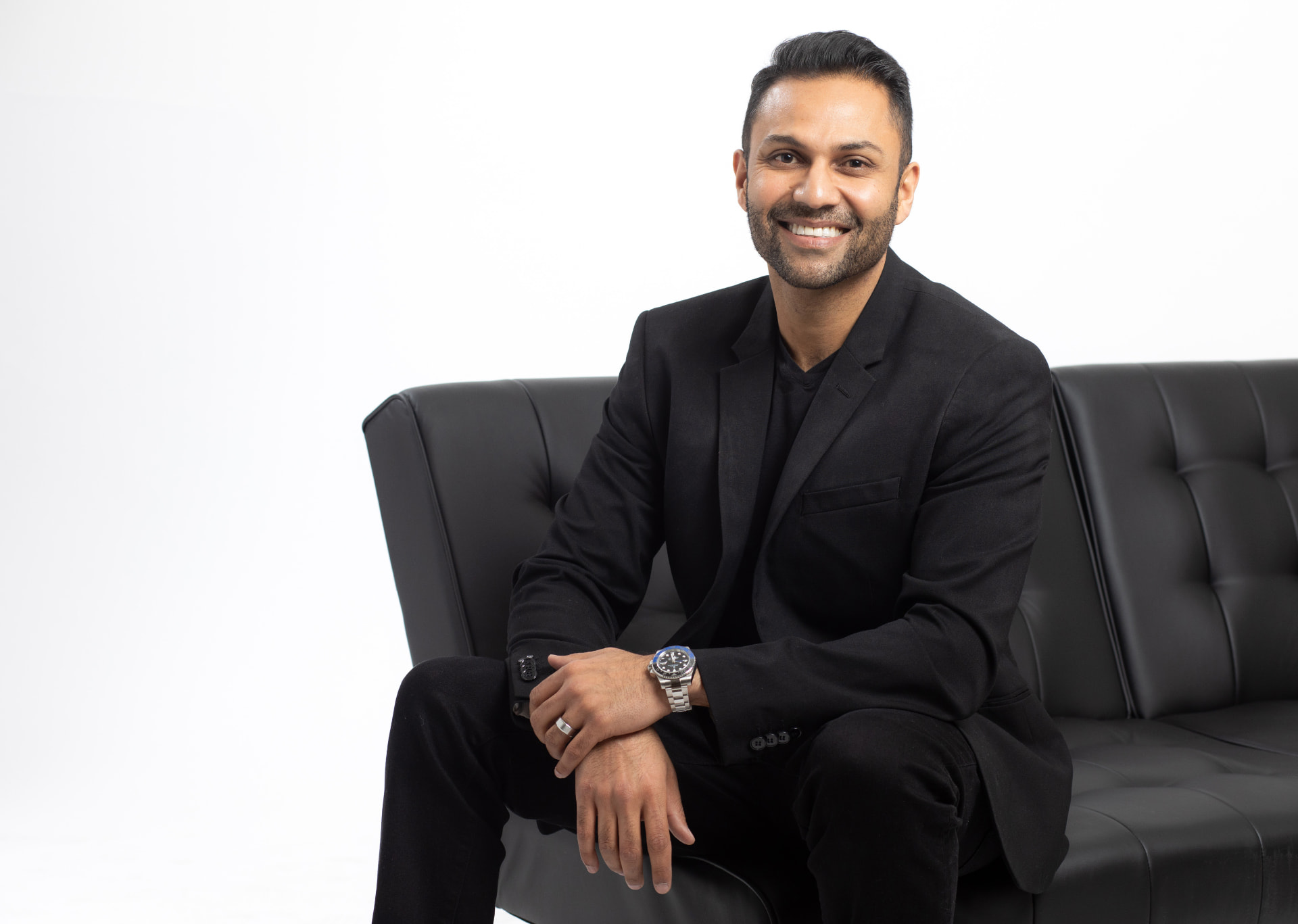 Executive in a black suit seated on a leather sofa against a white studio backdrop