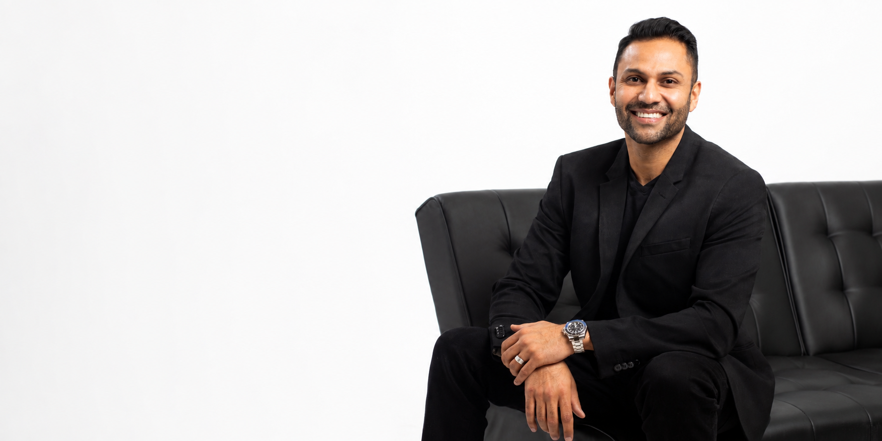 Executive in a black suit seated on a black leather sofa against a white studio backdrop